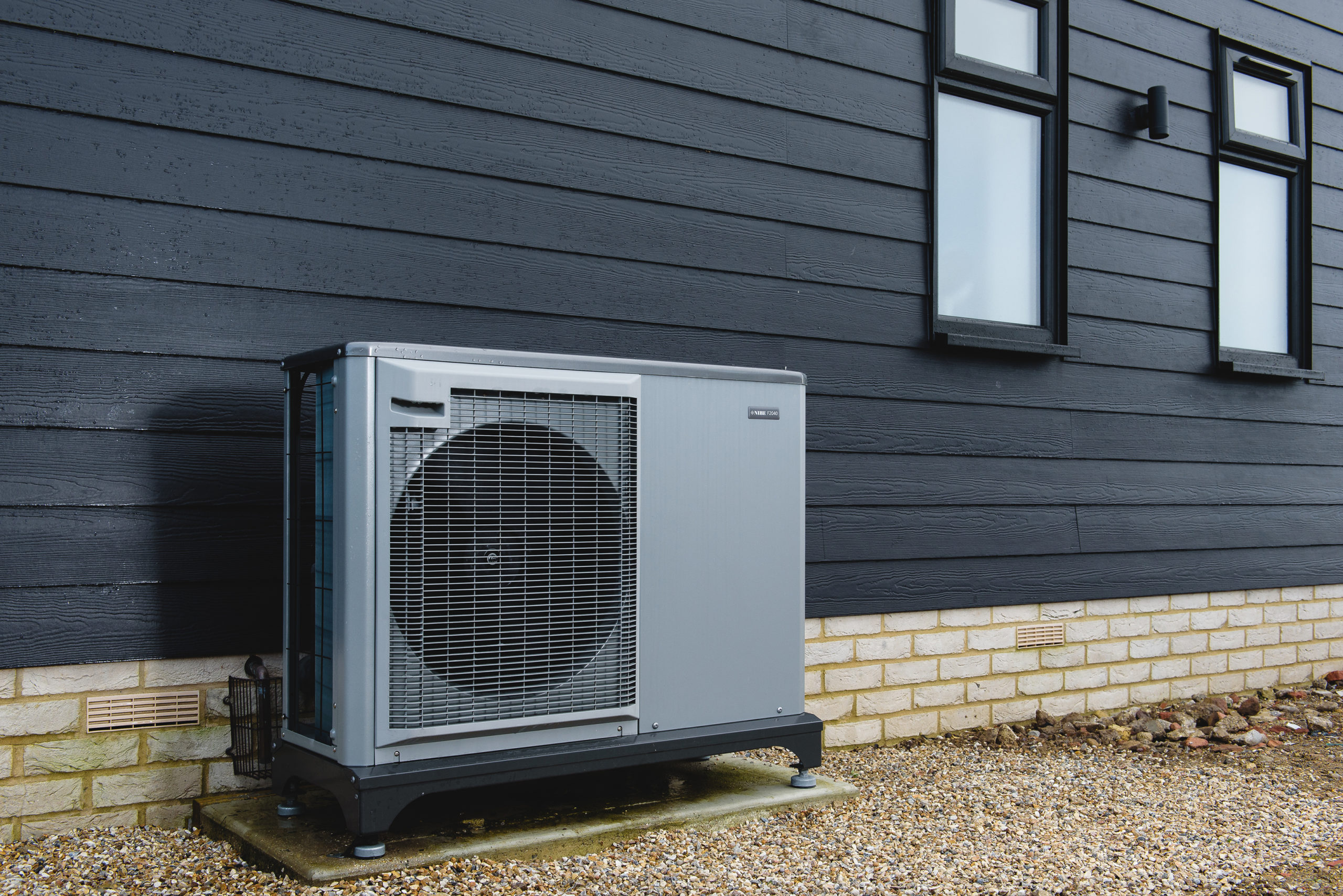 Air source heat pump installation completed. A grey ASHP next to dark building.