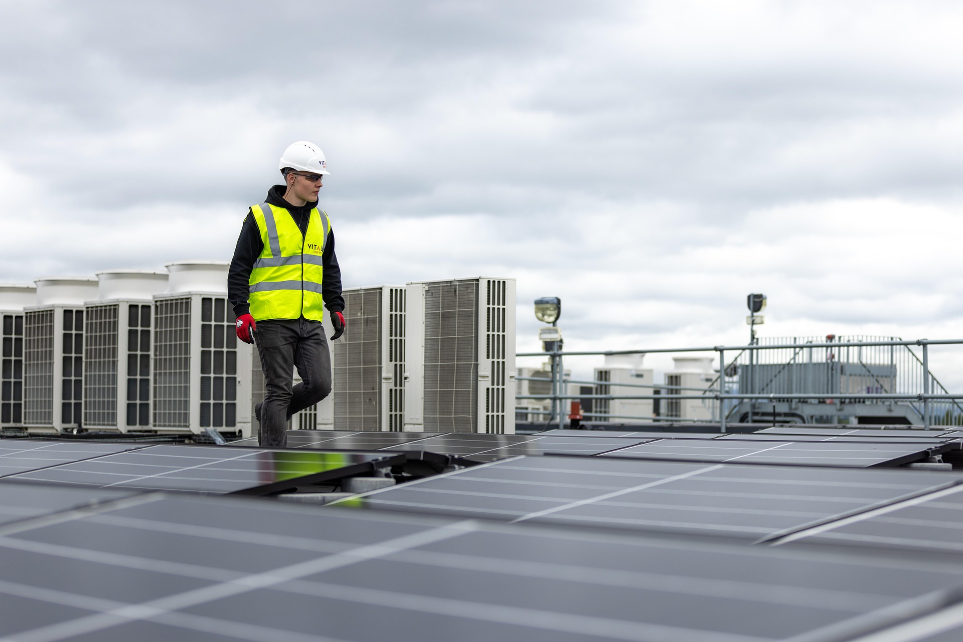 A man in a high vis vest on roof fitting commercial solar panels.
