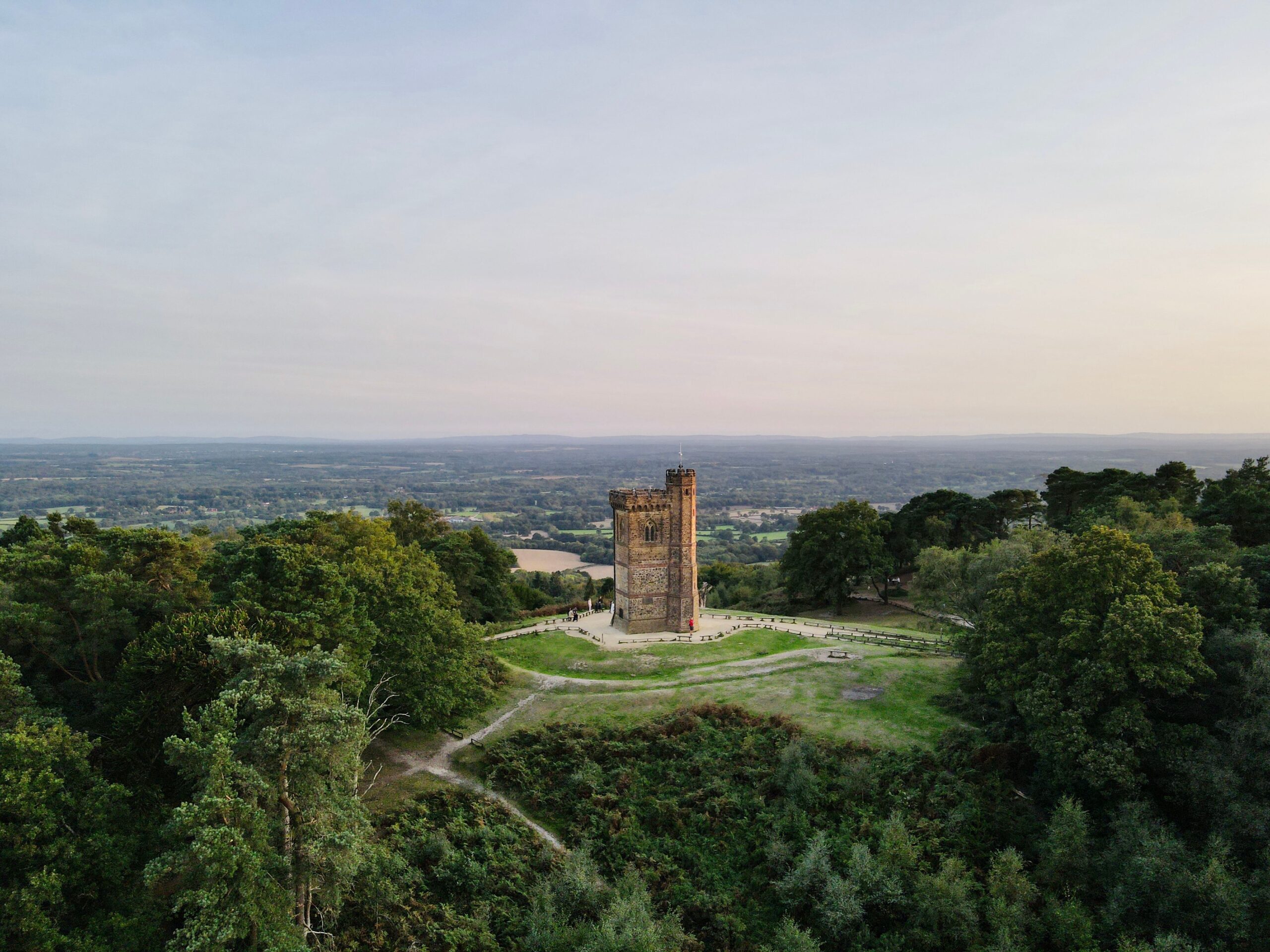 Leith Hill Tower surrounded by lush forest in Surrey, England at sunset.