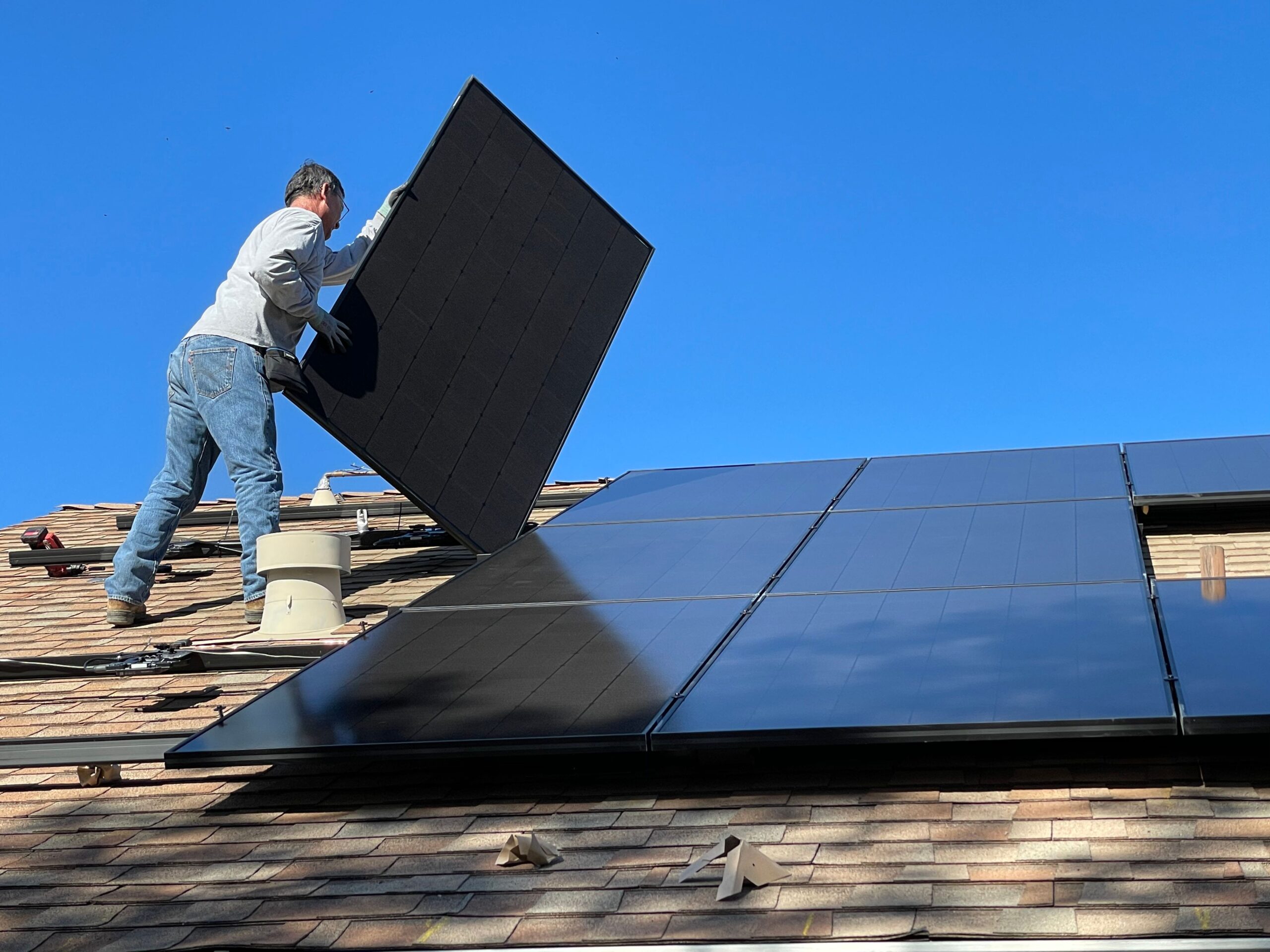 A man moving solar panels on a roof.