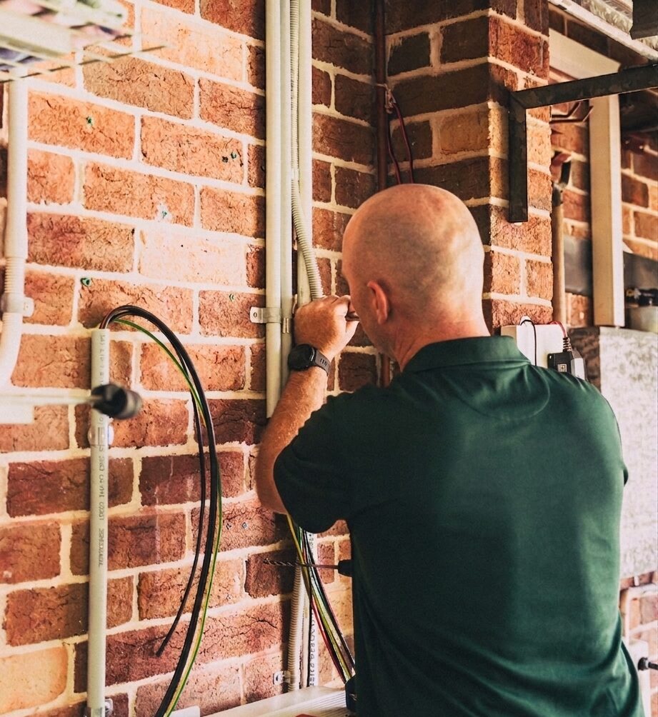 A bald man wearing a green polo shirt installing a solar battery.